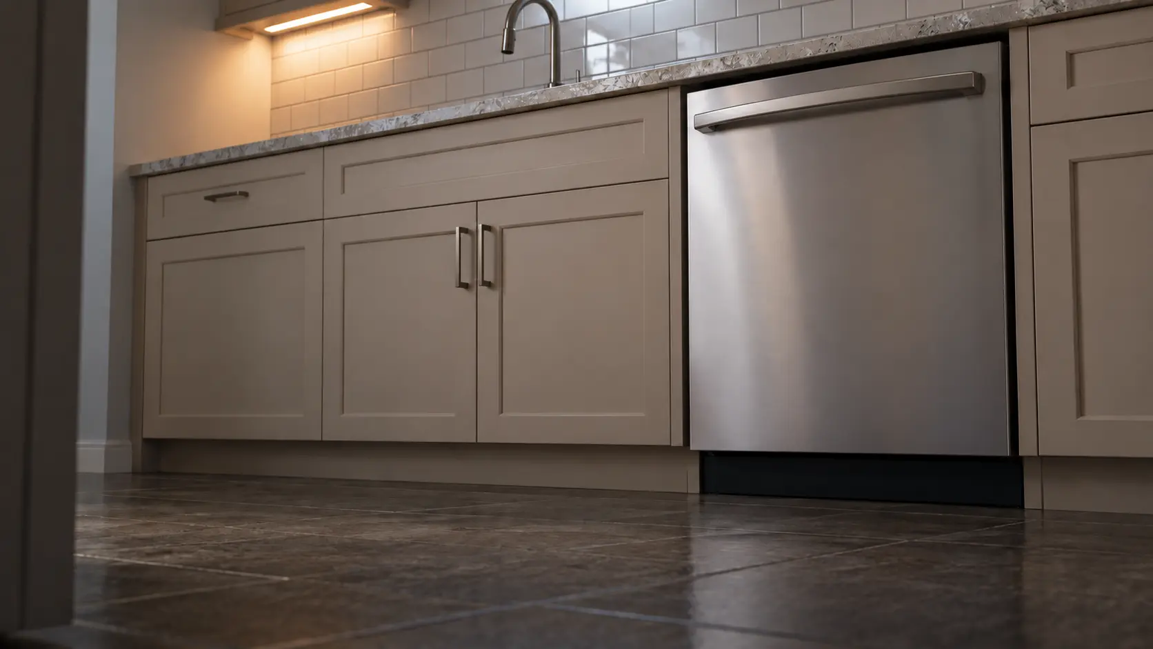 A dishwasher in a compact apartment kitchen with tiled walls and a single run of units.