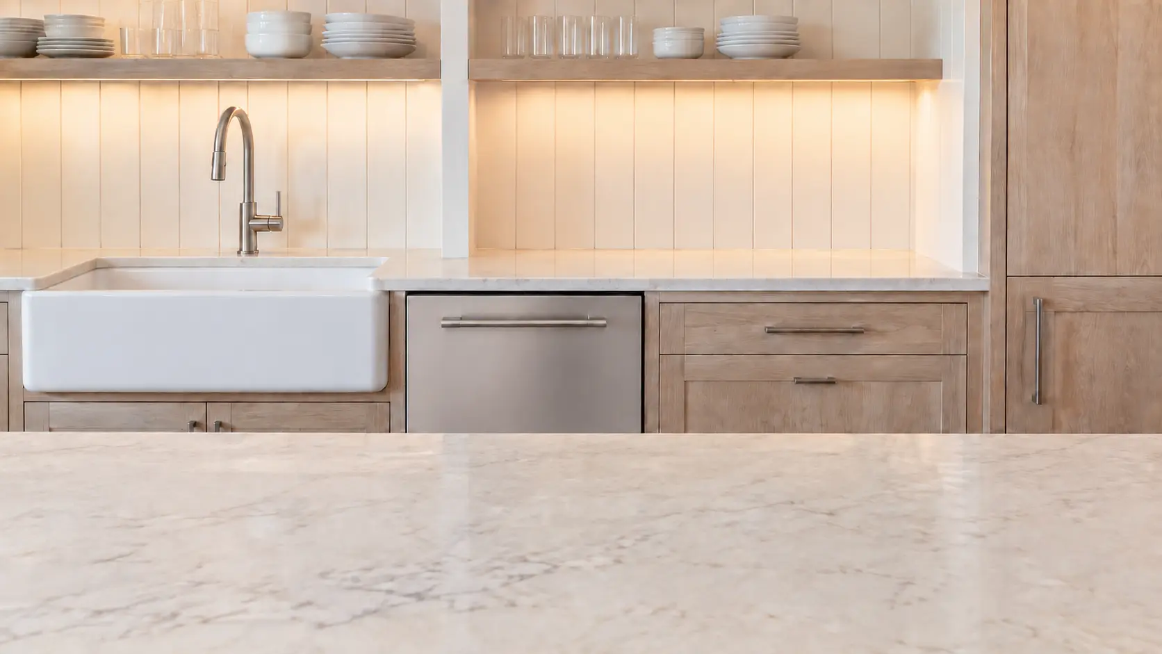 A dishwasher in a beach-house kitchen in whitewashed timber with open shelving.