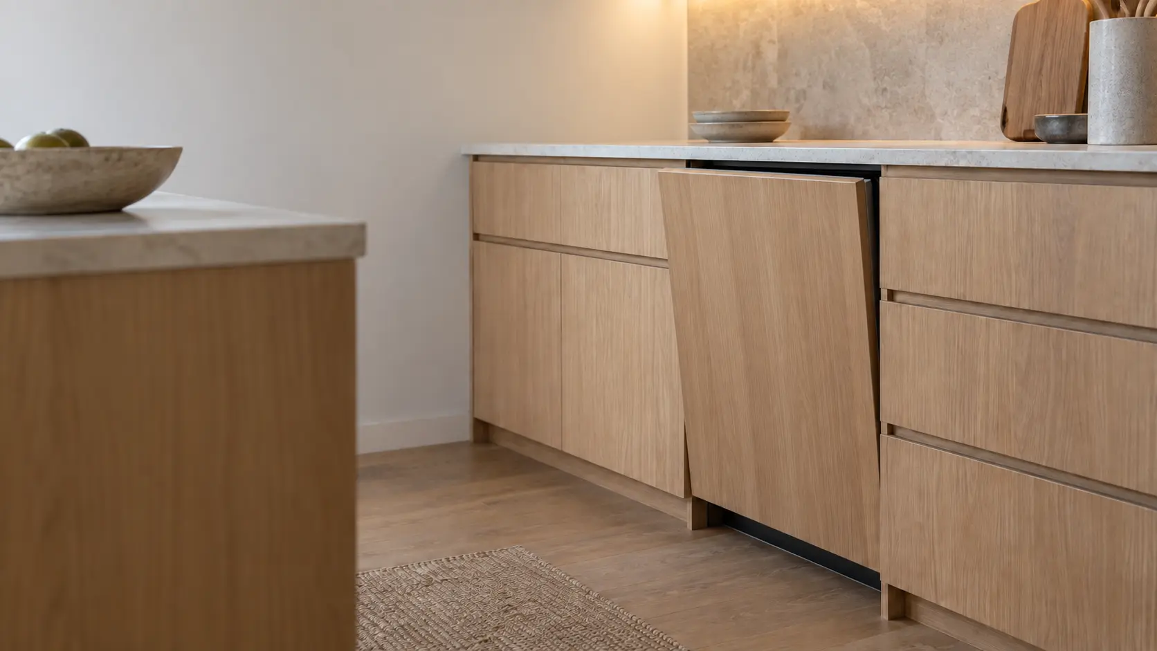 An integrated dishwasher door stands open in a run of painted shaker cabinets in a US home kitchen.