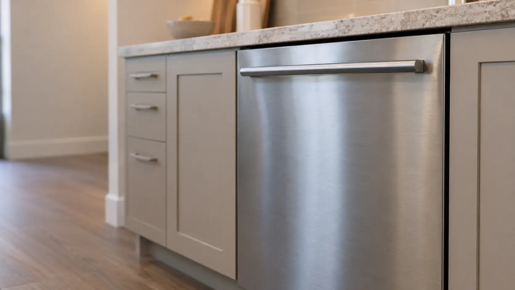 The brushed stainless door of a dishwasher filling the frame, its handle catching soft light.